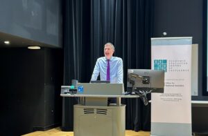 Sir Robert Chote stood behind a desk talking and addressing the room.