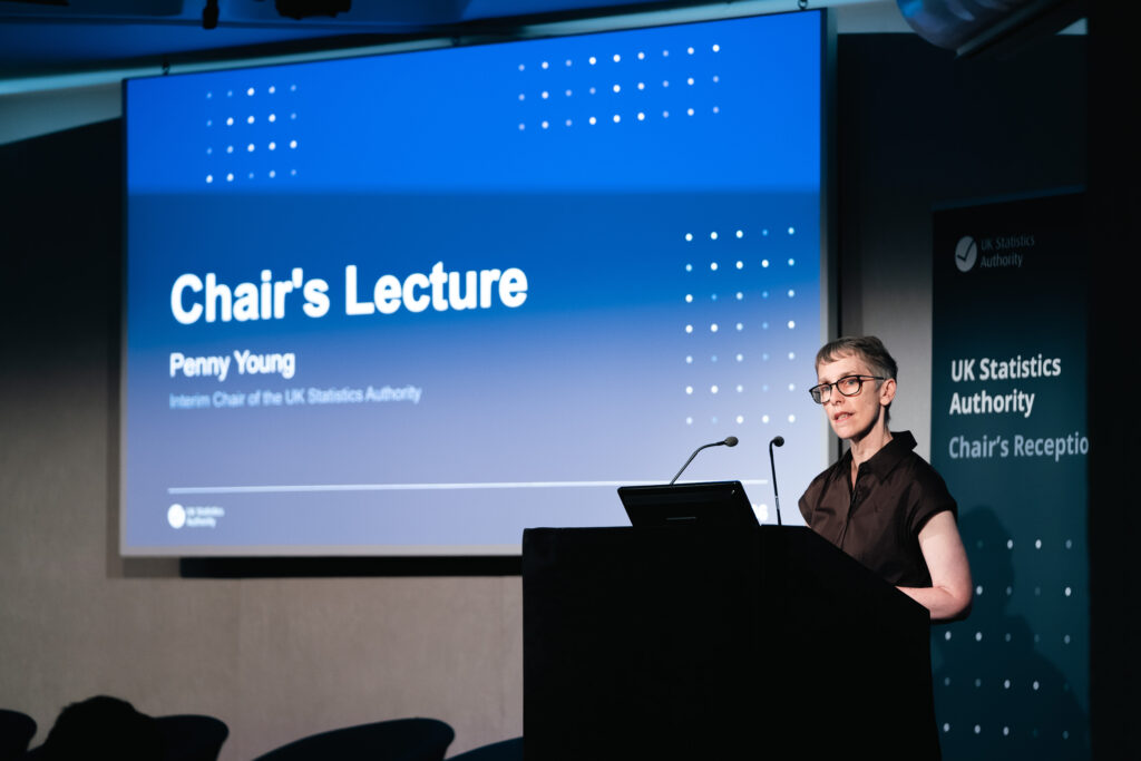 Penny Young stood at lectern in front of presentation slide that reads Chair's lecture.